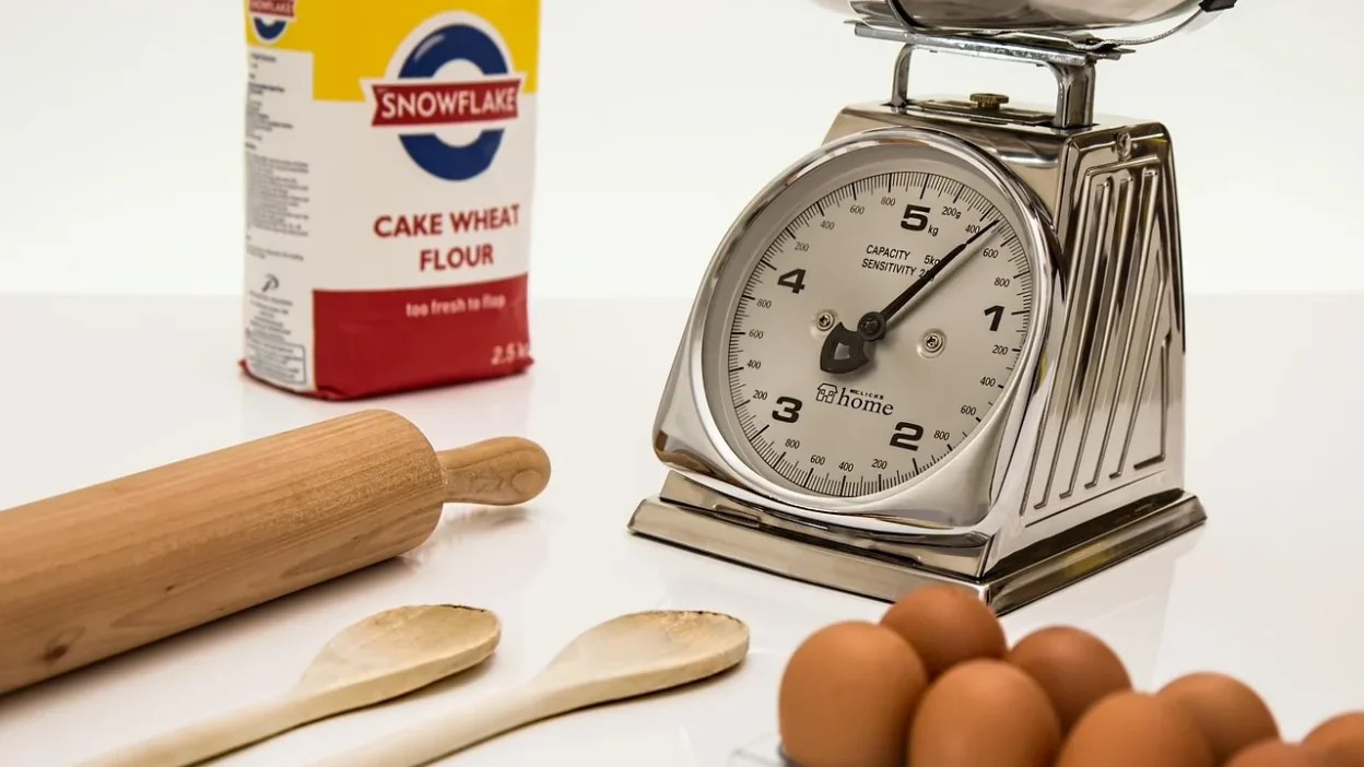 A digital kitchen scale measuring flour in grams next to a measuring cup, comparing accuracy for portion control.