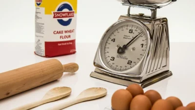 A digital kitchen scale measuring flour in grams next to a measuring cup, comparing accuracy for portion control.