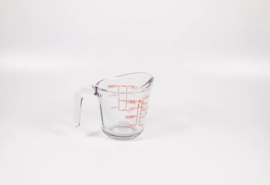 A clear glass measuring cup with red measurement markings, full of brown dry dog food kibble.