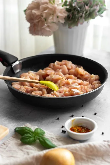 Raw chicken breast pieces seasoned with herbs in a black frying pan on a kitchen counter.